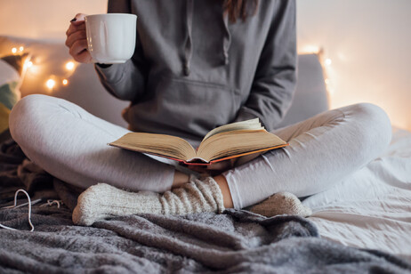 Una giovane sul letto con tisana calda e libro aperto foto iStock.